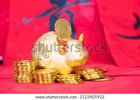 Gold coins and golden calf piggy bank on red background.The Chinese characters in the picture mean: "to attract wealth and treasure"