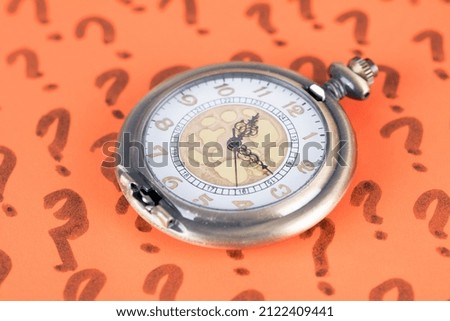 A pocket watch on a background full of question marks