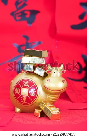 Gold bull piggy bank on festive red background carrying gold nuggets.The Chinese characters in the picture mean: "to attract wealth and treasure"