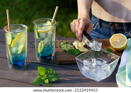 Girl makes summer refreshing cocktails blue lagoon. Close-up of adding ice cubes to glasses. Selective focus