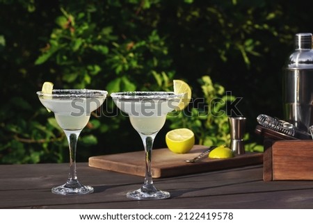Two glasses with fresh homemade margarita cocktail on a wooden table on a patio summer evening, selective focus Royalty-Free Stock Photo #2122419578