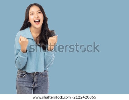 Excited young asian female with raised hands celebrating success Portrait cheerful positive asian woman with raised hands and fists open mouth Girl get happy Pastel blue background, copy space Royalty-Free Stock Photo #2122420865