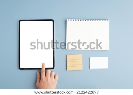 Hand touch digital tablet with blank on screen and blank notebook paper isolated on blue background, banner for template, mock up, topview, flat lay, communication technology