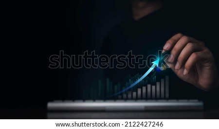 Investment technology, financial, return on investment - ROI concepts. Increasing arrow, the exponential curve of progress in business performance over charts draws by pen in hand on dark background. Royalty-Free Stock Photo #2122427246