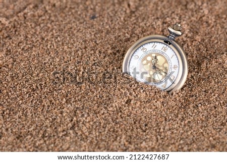 A pocket watch in the sand symbolizes the passage of time