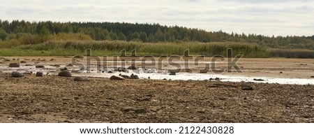 The drying bottom of the river against the background of a natural landscape - shore, trees, sky - nature banner Royalty-Free Stock Photo #2122430828