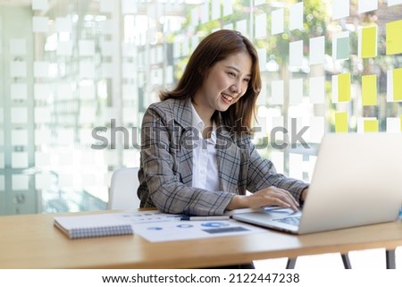 A businesswoman is checking company financial documents and using a laptop to talk to the chief financial officer through a messaging program. Concept of company financial management. Royalty-Free Stock Photo #2122447238