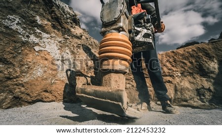 Worker uses a portable vibration rammer at construction of a power transmission substation Royalty-Free Stock Photo #2122453232