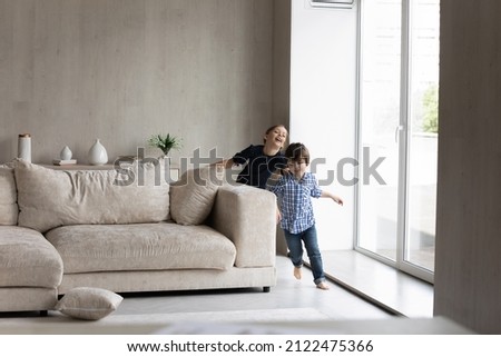 Happy excited two kids playing active games at home, running in living room, chasing each other, laughing, making noise. Sibling children having fun, enjoying entertainment in apartment for family Royalty-Free Stock Photo #2122475366