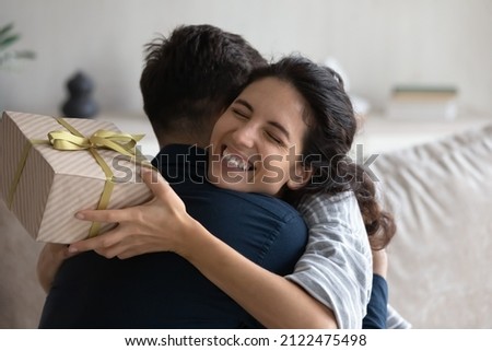Grateful happy young woman holding festive wrap, hugging beloved husband, boyfriend, thanking for present. Sweet millennial couple celebrating anniversary, 8 march, birthday, exchanging gifts Royalty-Free Stock Photo #2122475498