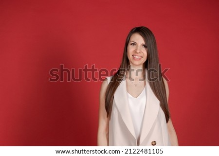 Half-length shot brunette business woman, satisfied after conference, happy looking at the camera, elegant light pink suit, models on a red background. Pleased female manager posing indoors