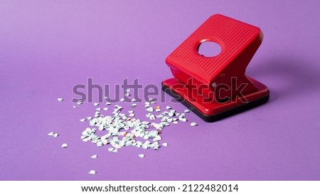 Red confetti maker. Hole puncher machine. Paper punch sprinkle. Hole punch art. Red puncher on violet background Royalty-Free Stock Photo #2122482014