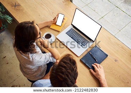 Overhead picture of two people looking at blank laptop  and smartphone screen sitting at cafe