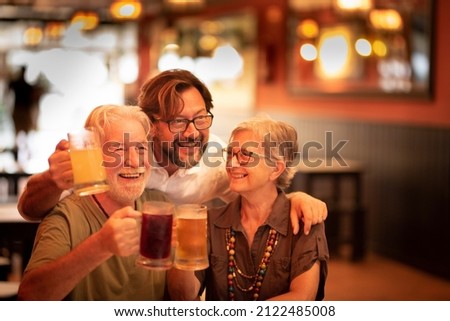 Happy family mixed generations adult and old senior people enjoy celebrating together clinking beers in a restaurant pub and looking for a nice picture