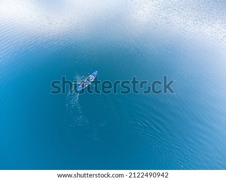 Aerial view of a couple canoeing in blue calm waters in the middle of the ocean. Drone view