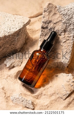 Glass bottle of moisturizing face serum, cosmetic oil on stones on a sandy background. Summer facial skin care concept. 