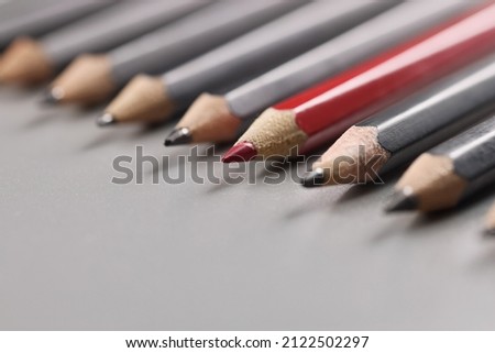 Pencils tips put on grey surface in strict order, red one among black pens