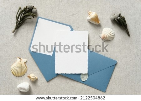Nautical wedding invitation card mockup with blue envelopes, flowers, seashell on beige table. Flat lay, top view, copy space. 