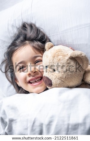 Little cute girl in bed with a teddy bear early in the morning.