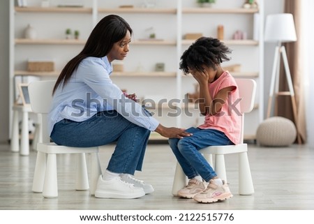 Distressed little black kid crying at psychotherapy session, beautiful young african american woman comforting emotional curly girl preschooler, clinic interior. Childhood stress concept Royalty-Free Stock Photo #2122515776