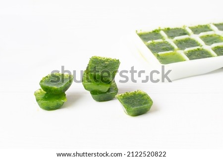 spinach ice cubes on a white table. frozen greens cubes.