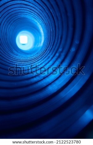 Neon swirl. Blur light background. Futuristic illumination. Fluorescent tunnel. Defocused led blue color glow rays in round grooved texture pipe on dark black.