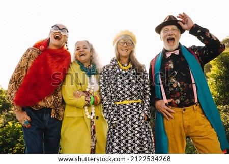 Group of eccentric mature friends laughing happily while standing together in a park. Stylish elderly people wearing colourful casual clothing. Carefree senior citizens enjoying life after retirement. Royalty-Free Stock Photo #2122534268