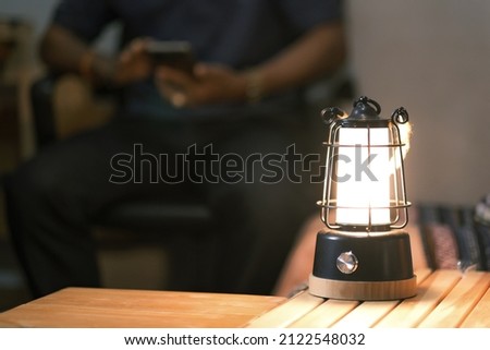 Led camping lamp on the wooden table, Man nice couple having fun on camping with kerosene lamp, sitting on a smartphone. Royalty-Free Stock Photo #2122548032