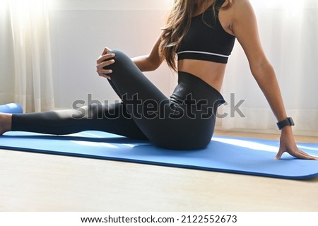 A cropped view portrait of a young  fit woman stretching her body on a mat in a studio , for home exercise, yoga and a class concept.