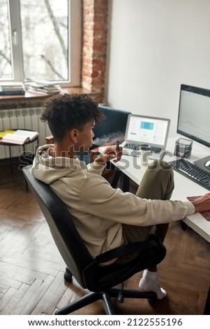 Thoughtful african american broker analyzing stock graph on pc screens and vaping. Working distantly. Stock exchange trader working distanly. Vaping electronic device.