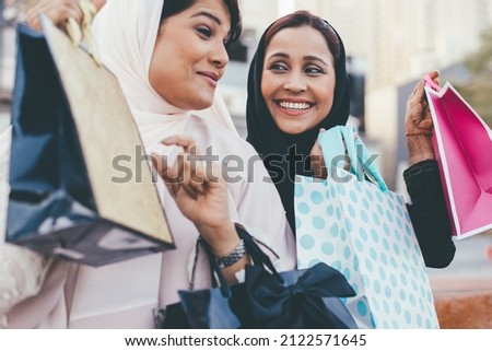 Two young women spending time together outdoor making activities. Two friends wearing the traditional emirates abaya dress making shopping in Dubai Royalty-Free Stock Photo #2122571645