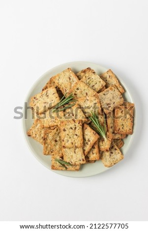 Square diet cookies with rosemary, flax seeds and spices  in a light plate on white background. Crunchy herbal crackers top view Royalty-Free Stock Photo #2122577705