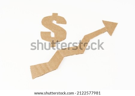 The concept of economic growth. On a white surface, a graph with an up arrow and a dollar symbol. Symbol, arrow and graph are made of cardboard