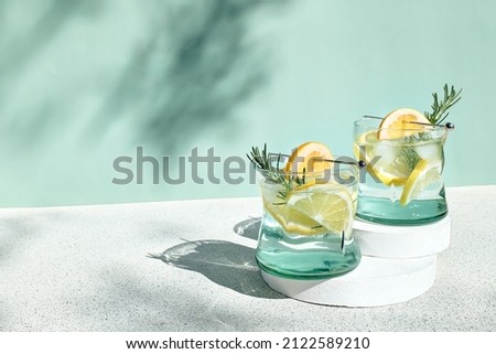 Summer refreshing lemonade drink or alcoholic cocktail with ice, rosemary and lemon slices on pastel light green surface. Fresh healthy cold lemon beverage. Water with lemon. Royalty-Free Stock Photo #2122589210