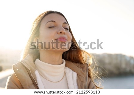 Young charming woman breathing fresh air relaxing and smiling with closed eyes at sunset