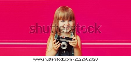 Portrait of little girl child with vintage film camera taking picture on pink background