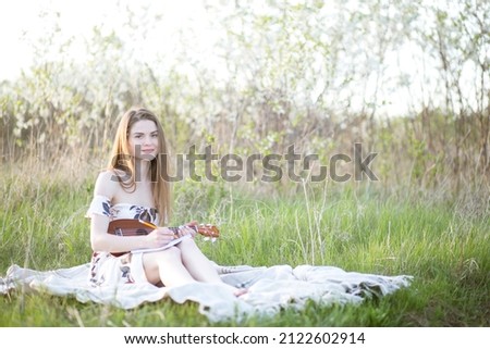 A girl on green grass plays guitar .