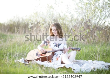 A girl on green grass plays guitar .