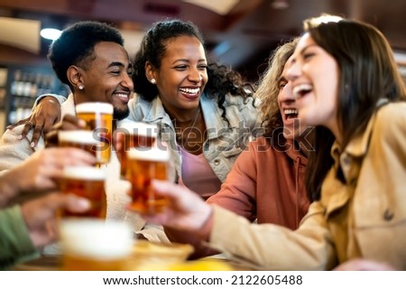 Group of smiling friends drinking and toasting beer at bar restaurant - Friendship concept with young happy people having fun together toasting brew pint on happy hour Royalty-Free Stock Photo #2122605488