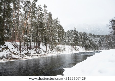 A beautiful landscape with a mountain river, snow and forest in Arkhyz, on a cloudy winter day. Caucasus Mountains,  Russia.
