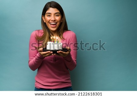 Beautiful latin woman laughing while holding her birthday cake with candles in front of a blue background
