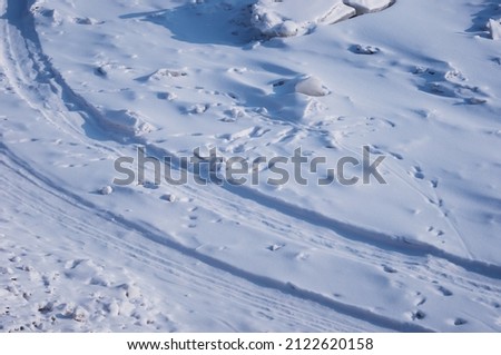 Ski track on the snow-covered ice of the river. Fragments of ice. Footprints after a snowfall. Glitter of snowflakes and smooth morning shadows. Path of the border patrol on the state border.
