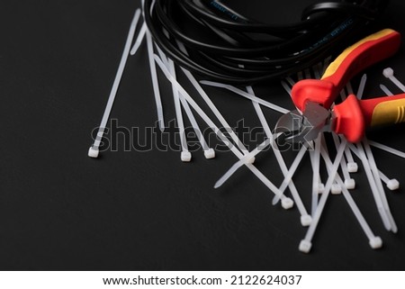 wire cutters with electric cables and cable ties on a black background with a place for the inscription Royalty-Free Stock Photo #2122624037