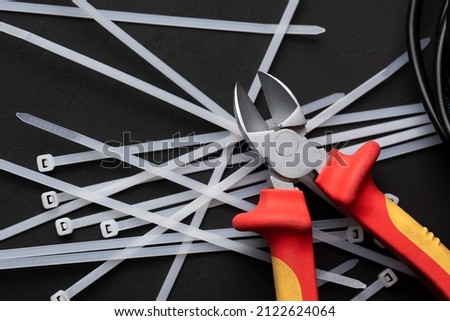 wire cutters with electric cables and cable ties on a black background with a place for the inscription Royalty-Free Stock Photo #2122624064