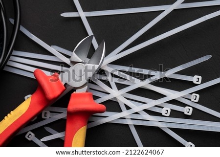 wire cutters with electric cables and cable ties on a black background with a place for the inscription Royalty-Free Stock Photo #2122624067