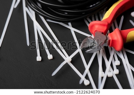 wire cutters with electric cables and cable ties on a black background with a place for the inscription Royalty-Free Stock Photo #2122624070