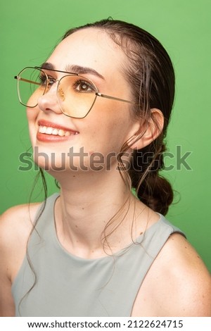 Portrait of smiling young woman with gathered dark hair in glasses isolated on green