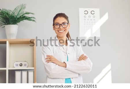 Portrait of happy young Caucasian female optician in white medical uniform pose in optics salon. Smiling woman doctor in private clinic or hospital. Eyesight correction. Healthcare, sight problem. Royalty-Free Stock Photo #2122632011