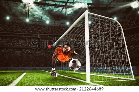 Goalkeeper in orange uniform catches the ball in the stadium during a football game Royalty-Free Stock Photo #2122644689
