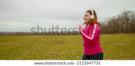 Fat woman in sportswear and wireless headphones running in the park. Healthy lifestyle concept. Active sport
